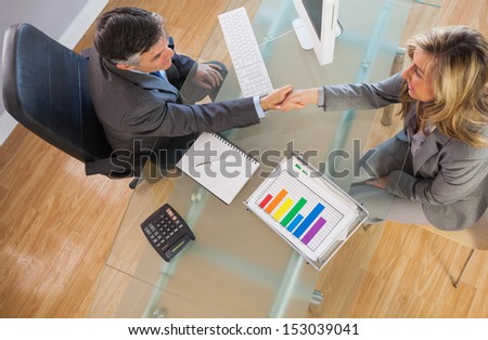 A Businessman Shaking The Hand Of A Businesswoman Above A Desk In An Office