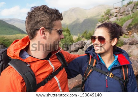 Couple wearing rain jackets and sunglasses smiling at each other in the countryside