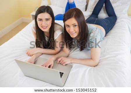 Smiling friends using a laptop lying on bed at home in bedroom
