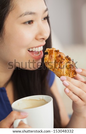 Young asian woman eating a pastry with a cup of coffee in living room at home