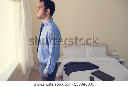 Frowning man standing looking out the window in a bedroom at home