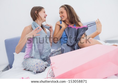 Teen girls sitting on bed after shopping and holding new clothes
