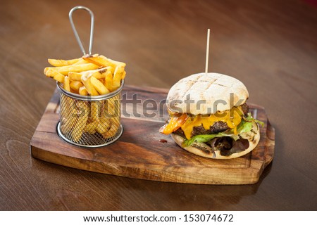 Close up on a cheese burger and french fries served in classy restaurant on a wooden board