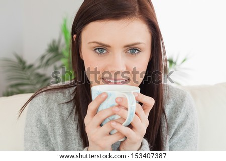 Smiling brunette drinking a cup of coffee at home looking at camera