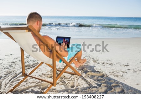 Handsome man scrolling on his tablet pc on the beach