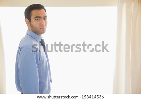 Stressed man looking at camera standing in front of a window in a bedroom at home