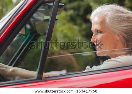 Smiling mature woman driving red convertible on sunny day