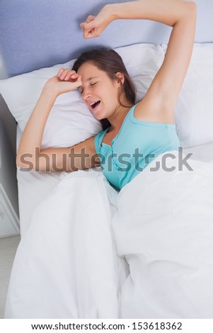 Well rested brunette woman stretching and yawning in bed in bedroom at home