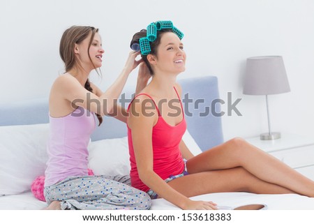 Girls sitting in bed and girl fixed her friends hair rollers at sleepover