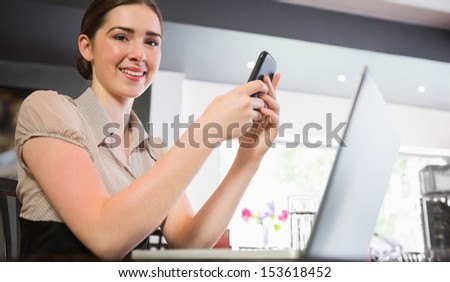 Smiling businesswoman holding phone looking at camera in a restaurant