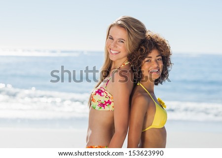 Smiling friends in bikinis standing back to back looking at camera