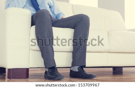 Low part of classy businessman sitting on cosy sofa in bright living room