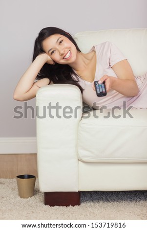 Happy asian girl lying on the sofa watching tv at home in the sitting room