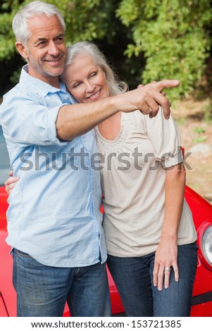 Smiling mature couple posing by their red convertible on bright day
