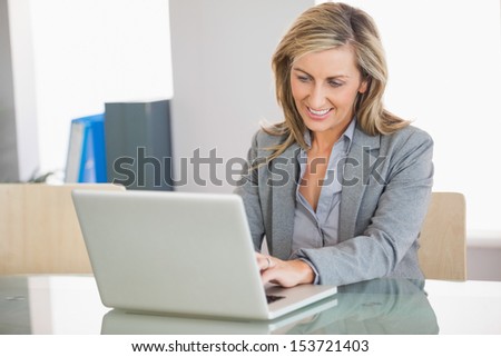 A smiling blonde businesswoman typing on a laptop in an office