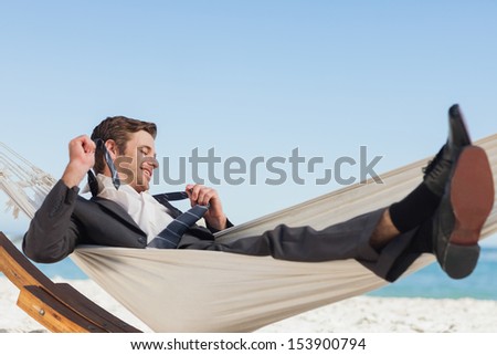 Smiling Businessman Lying In Hammock Taking Off His Tie At Beach