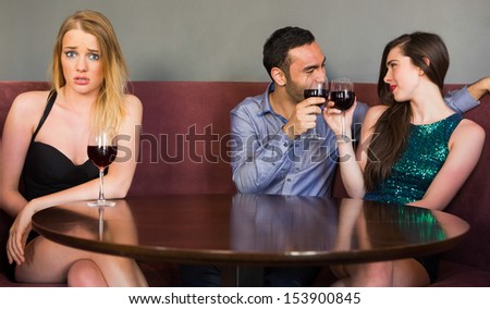 Blonde woman feeling jealous as two people are flirting beside her in a club looking at camera