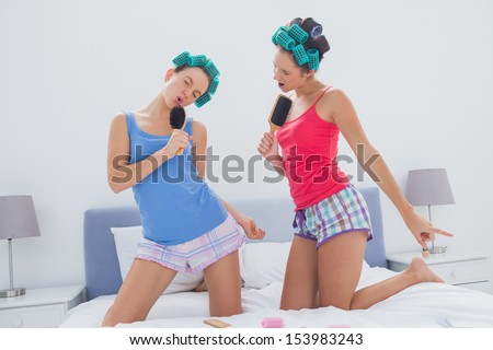 Girls in hair rollers singing with hairbrush in bed at sleepover