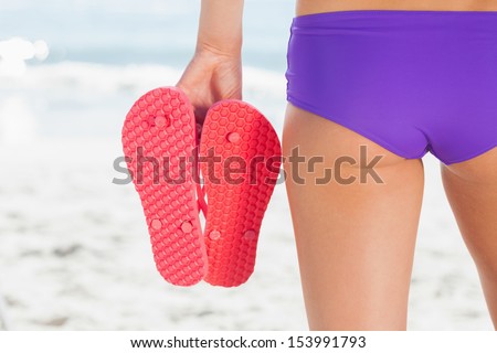 Rear view of a young woman holding flip flops while standing on the beach