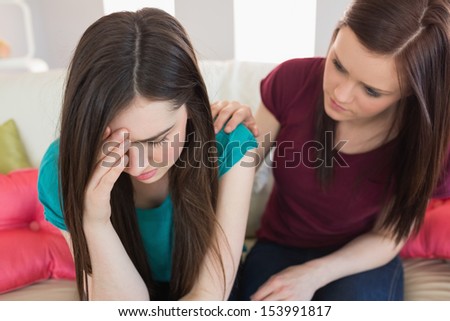 Girl comforting her crying friend on the couch at home in living room