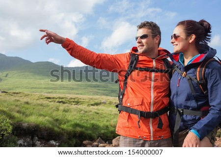 Couple wearing rain jackets and sunglasses admiring the scenery with man pointing in the countryside
