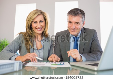Two pleased mature business people smiling at camera analyzing a graphic at office