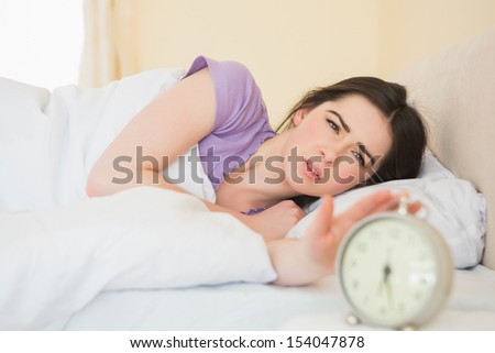Irritated girl waking up in her bed by an alarm