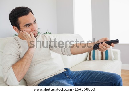 Handsome man on cosy sofa getting bored of tv programs