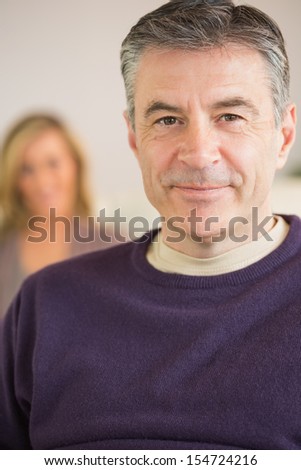Smiling mature man looking at camera with his wife blurred in the background