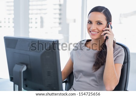 Cheerful dark haired businesswoman having a phone conversation in her office