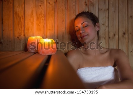 Happy brunette woman sitting in a sauna relaxing by candlelight Happy brunette woman sitting in a sauna relaxing by candlelight