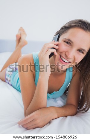 Woman lying in bed with phone and looking at camera