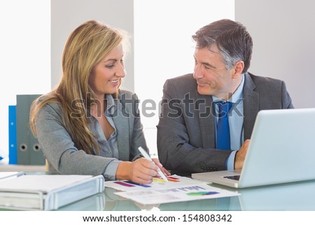 Two happy mature business people smiling to each other trying to understand figures at office