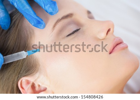 Surgeon making injection on crows feet on calm woman lying on operating table