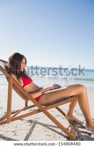 Woman on the beach using her laptop while relaxing on her deck chair
