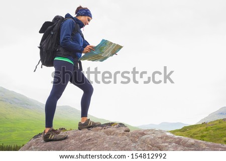 Woman standing on a rock reading map on hike in the countryside
