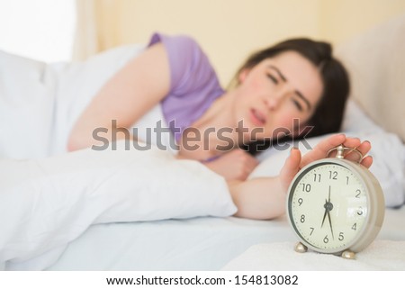 Upset brunette in her bed turning off her alarm clock