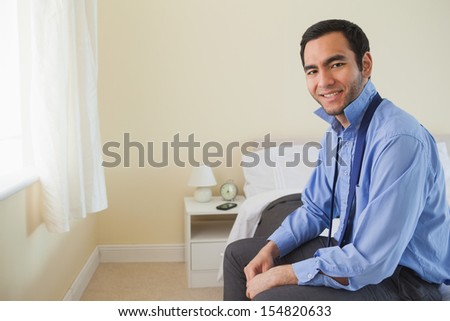 Pleased man looking at camera and relaxing sitting on his bed in a bedroom at home