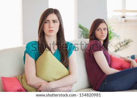 Two upset friends not talking to each other after fight on the sofa in sitting room at home