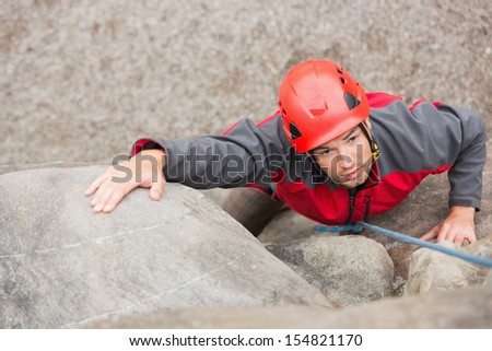 Determined man climbing rock face wearing red helmet