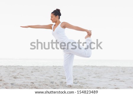Brunette woman wearing all white stretching in yoga pose at beach