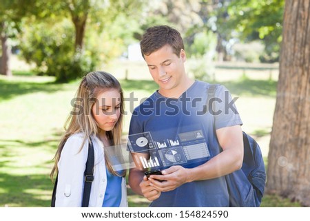 Smiling college friends using digital phone in bright park