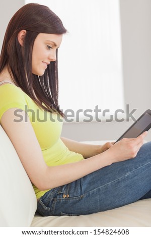 Pretty brunette looking and using a tablet pc sitting on a sofa