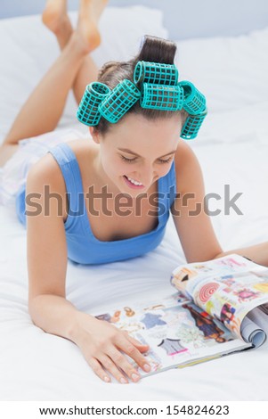 Smiling girls in hair rollers lying on bed and reading magazine