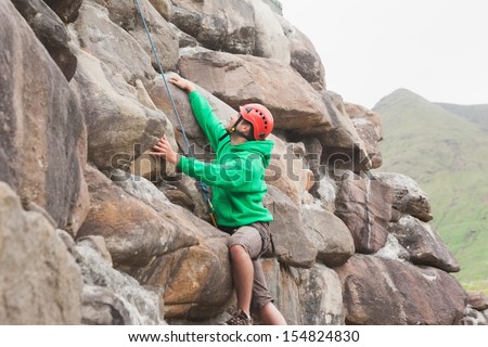 Fit man scaling a large rock face in the countryside