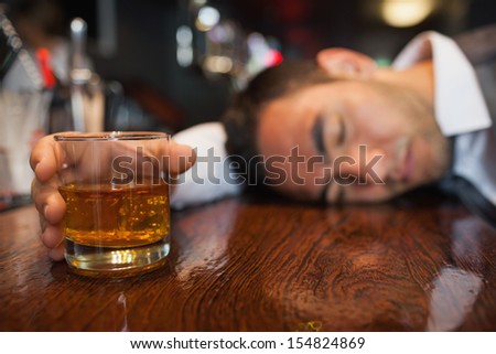 Drunk businessman with whiskey in his hand lying on a counter in a classy bar