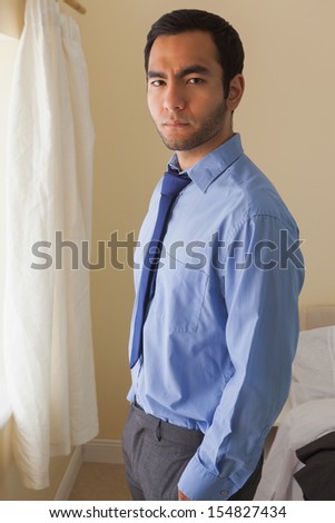 Angry man looking at camera standing in front of a window in a bedroom at home