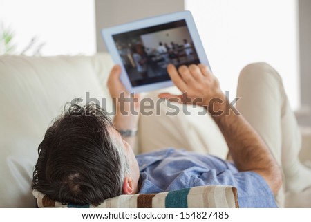 Mature man lying on a sofa in a living room using a tablet pc