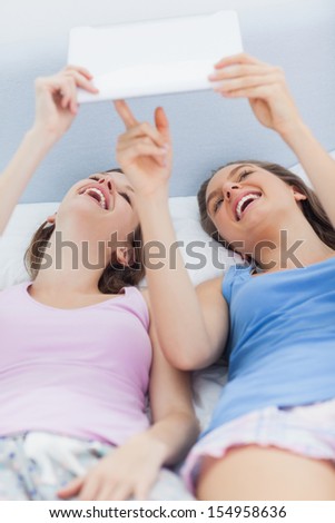 Girls lying in bed holding tablet and pointing to it at sleepover