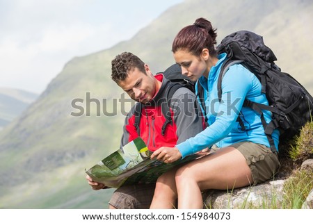 Couple resting after hiking uphill and reading map in the countryside